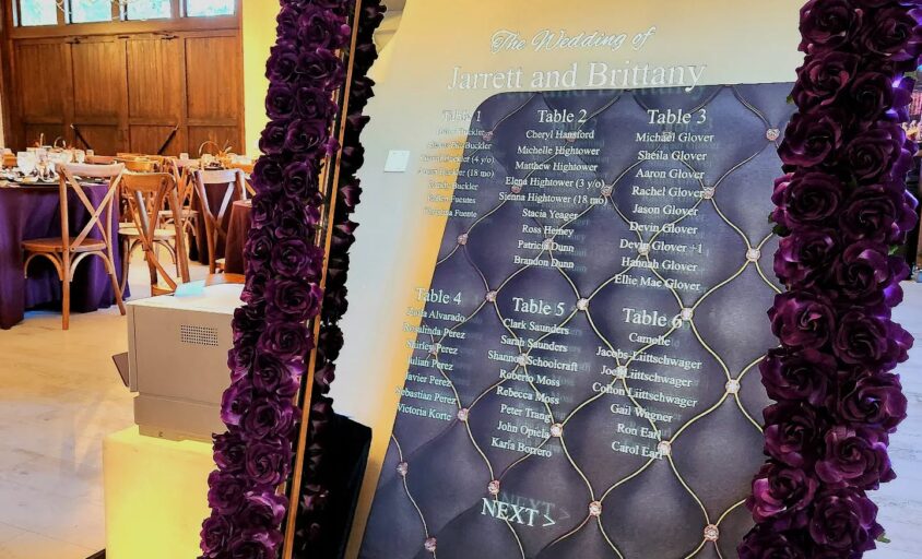 Mirror photo booth with a purple floral frame displaying a wedding seating chart
