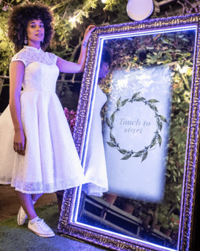 Guest standing beside an illuminated mirror photo booth at an evening event