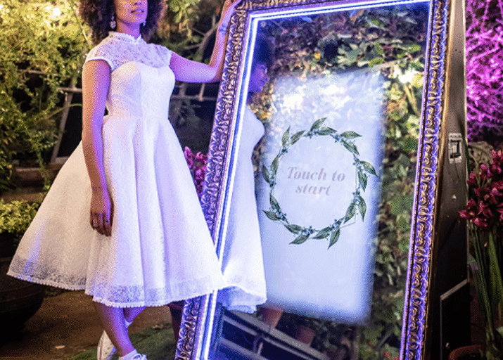 Guest standing beside an illuminated mirror photo booth at an evening event