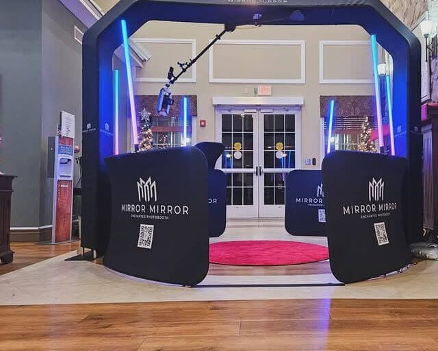 Sky 360 video booth with overhead camera, blue lighting, black barriers, and a pink floor mat at an indoor venue