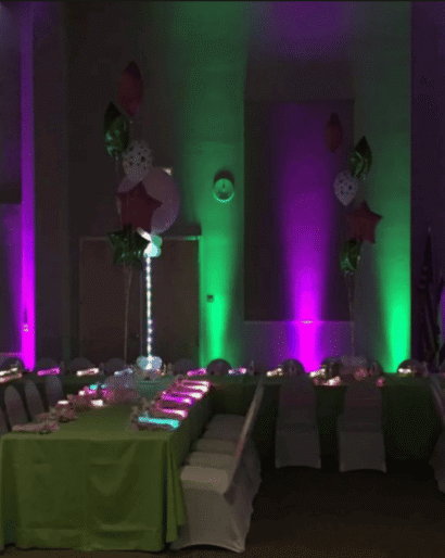 Green and purple event uplighting illuminating columns beside banquet tables