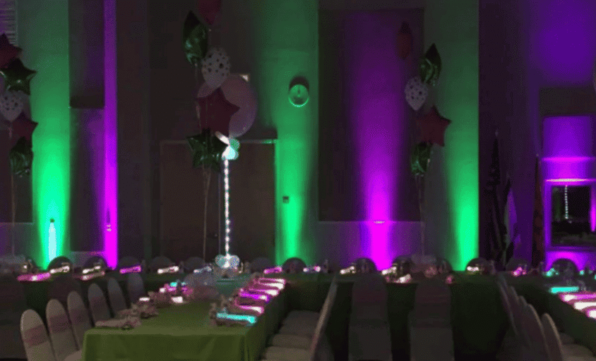 Green and purple event uplighting illuminating columns beside banquet tables