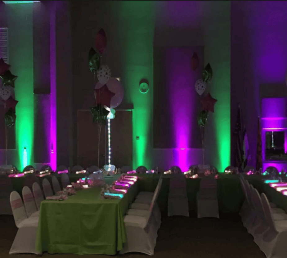 Green and purple event uplighting illuminating columns beside banquet tables